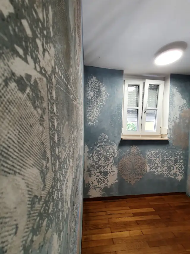 Blaugraue Wand mit hellen Ornamenten neben einem Treppenhausfenster